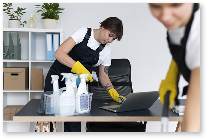 Addetta al cleaning mentre sanifica scrivania e laptop in ufficio – servizio professionale di facility management